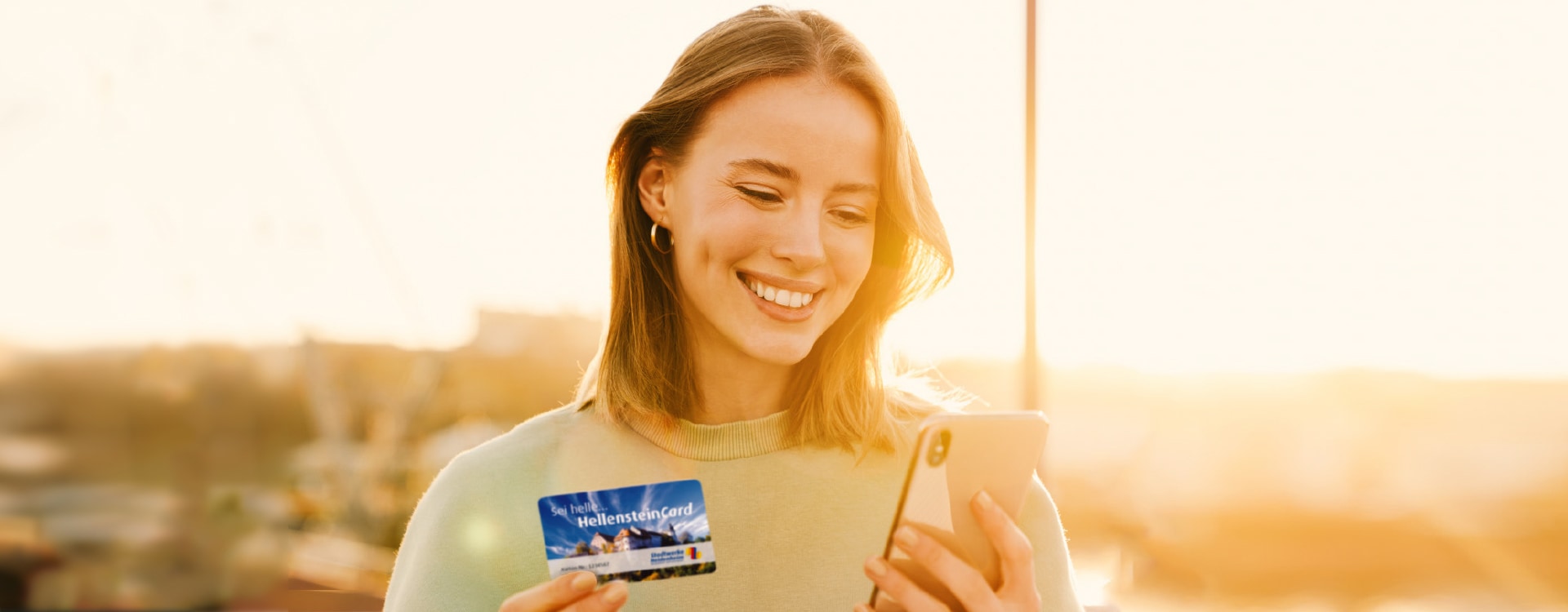 Junge Frau mit einer HellensteinCard und einem Smartphone in den Händen